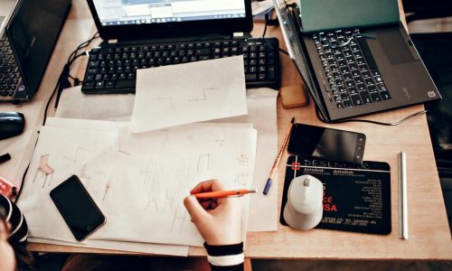 Top view of a business workspace with sketches, laptops, and drawing tools.